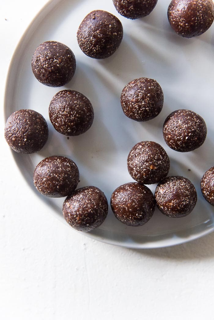 Smooth balls of fudgy chocolate chia bliss balls kept on a white plate on a white table top. 