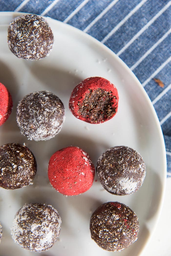 An overhead view of the chocolate chia bliss balls, that are coated with coconut, strawberry powder on a white plate. 