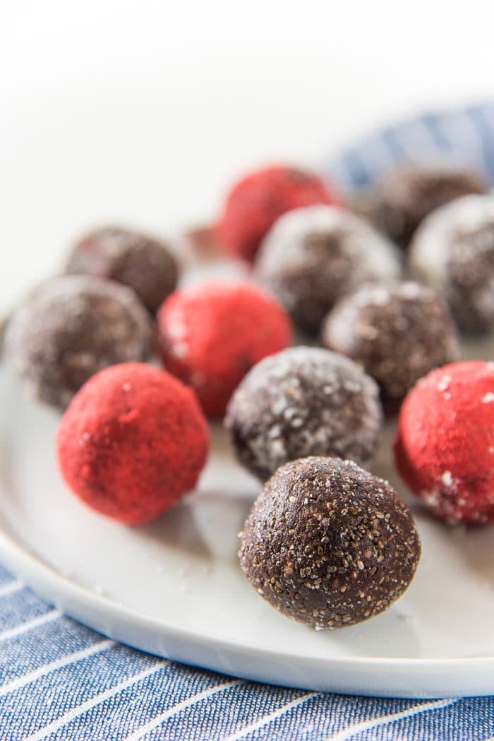 Uncoated, coconut coated and strawberry powder coated fudgy chocolate chia bliss balls on a white plate, with a blue napkin underneath.