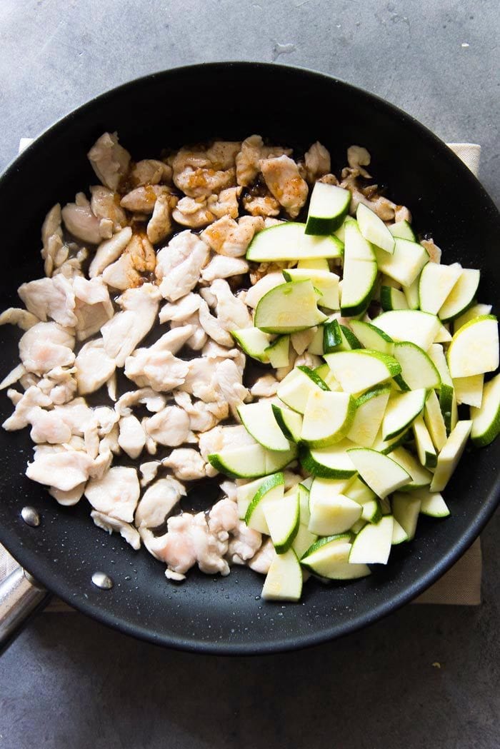 Cooked chicken in a large skillet, with the stir fry sauce and zucchini added.