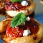 Puff pastry cherry tomato tartlet topped with a basil leaf and goat cheese.