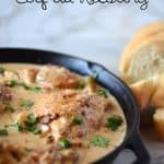 A skillet of creamy coq au riesling chicken dish garnished with parsley next to slices of crusty bread.