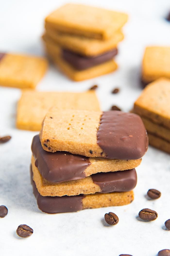 Chocolate dipped espresso shortbread cookies stacked on a white tabletop.