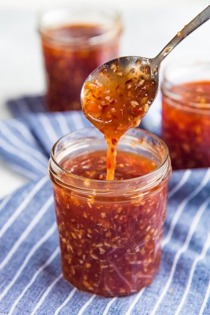 Spicy Sweet Chili Sauce in a jar, with a spoon pouring some sauce into the jar. 
