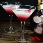 Two martini glasses with red, pink, white colored white chocolate cocktails with vanilla beans as garnish.