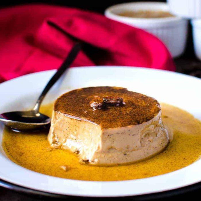 Coffee flan with caramel sauce unmolded onto a white plate and served with a spoon.
