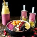 Yellow and pink mango peanut butter smoothie in a bowl, bottle, and two smoothie popsicles.