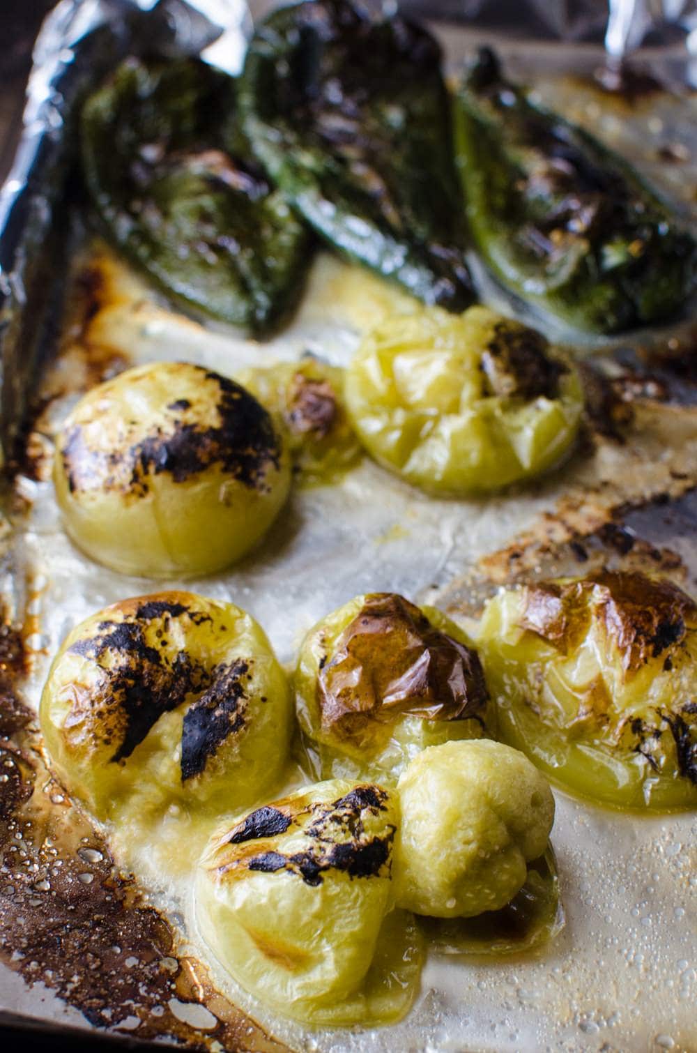 Tomatillos and poblano peppers that have been roasted and charred on a foil lined baking tray