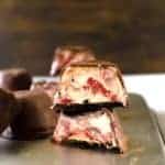 Two chocolate covered frozen cheesecake bites stacked on top of each other.
