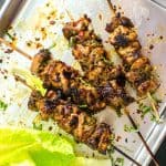 Four spicy Thai chicken skewers on a sheet pan with romaine lettuce leaves next to them.