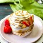 A swirled and lightly torched mini baked alaska dessert topped with thin strawberry slices, sits on a white plate.