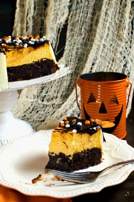 Brownie Bottom Pumpkin Cheesecake With Chocolate Fudge Sauce - A delicious combination of Fudgy brownies and creamy Pumpkin cheesecake in one dessert! Dress it up for Halloween or keep it simple to celebrate Thanksgiving or Fall. A great twist on Brownie Bottom Cheesecake with Fall flavors and Halloween cheer!