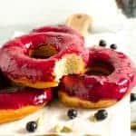 Three blueberry glazed doughnuts with a bite taken out of one to show the fluffy texture inside.