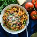 Bowl of spicy Tuscan sausage pasta with cannellini beans, olives, grated cheese etc. on top.