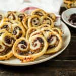 A plateful of puff pastry savory palmiers showing the berry jam and cheese filling on top.