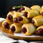 Stack of pigs in a blanket with cocktail sausages on a wooden serving platter.