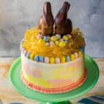 Colorful vanilla chai cake with Easter decorations and chocolate bunnies on top, on a cake stand.