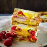 Stack of two ham and egg sandwiches on a white plate, with raspberries on the plate.