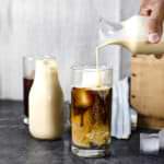 A hand pours cookie butter creamer into a glass with cold brew coffee, creating a swirling effect.
