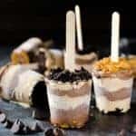 Creamy cookie butter chocolate fudge popsicles topped with crushed oreos and biscoff cookies on a dark surface.