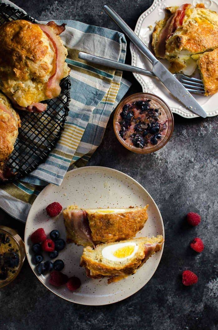 Bacon wrapped Egg Stuffed Breakfast Biscuits (Breakfast Scones) - Cheesy and herby buttermilk biscuits that are delightfully soft in the middle and extra flaky on the outside, and stuffed with a perfectly cooked egg and wrapped with bacon for good measure. Perfect for Brunch. 