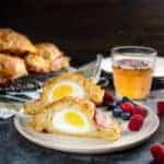 Egg stuffed bacon wrapped breakfast scone cut in half and served on a plate with fruits.