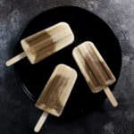 Three vanilla and chocolate protein popsicles on a black plate, against a black background.