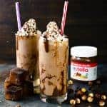 Two glasses of Nutella coffee slushie topped with whipped cream and Nutella sauce, served with straws.