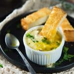Mushroom eggs en cocotte served in a small white ramekin with a spoon and piece of toasted bread.