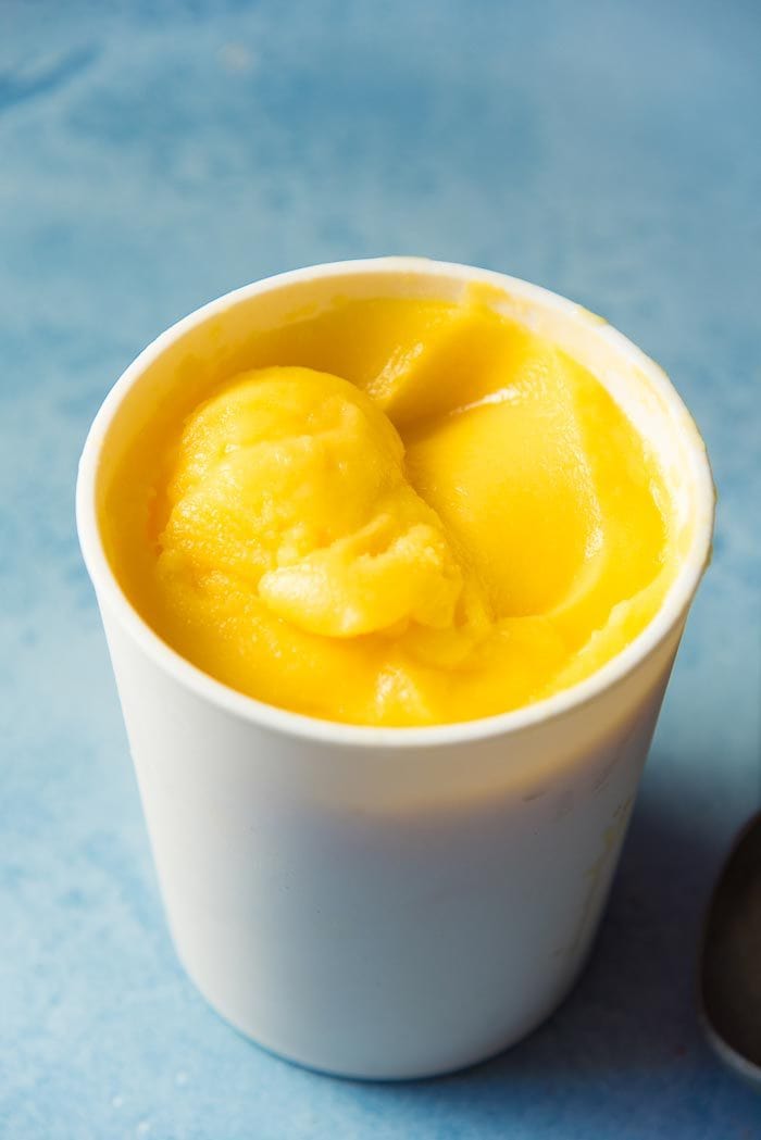 Frozen Mango Margarita in a white ice cream container on a blue table top.