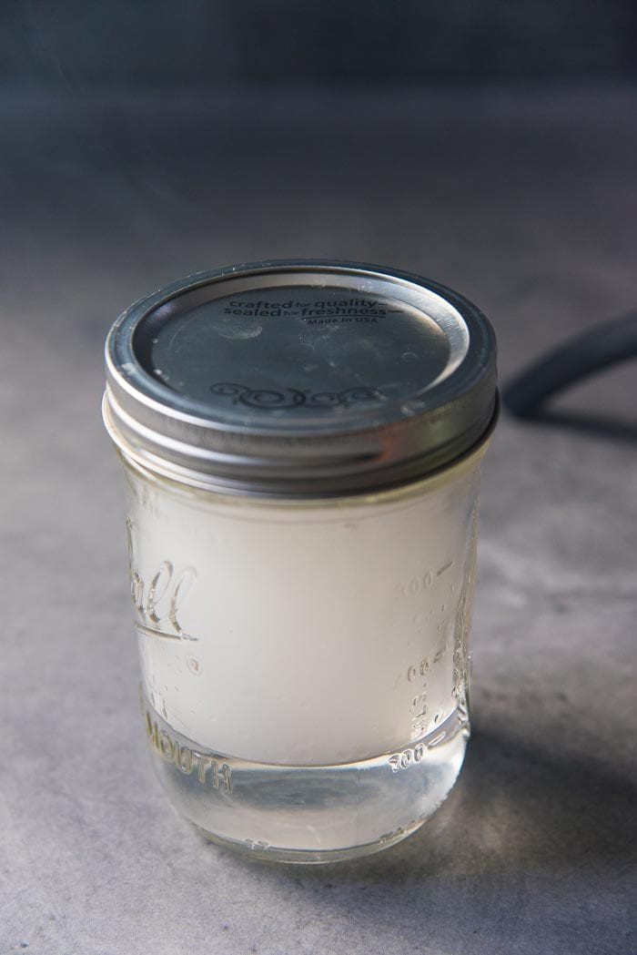 A mason jar closed with a silver lid, with clear silver tequila in the bottom and then filled with smoke.