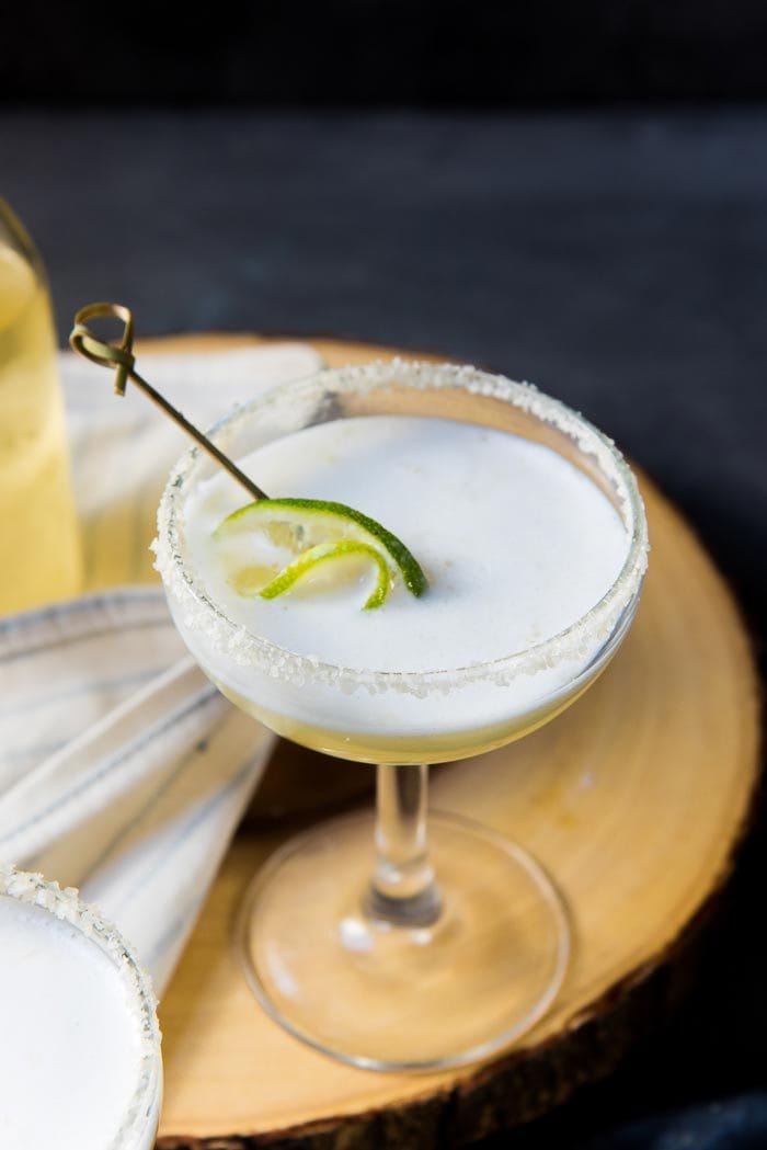 A close up of a smoked margarita sour, with the white foam created with aquafaba visible. A lime slice is placed in the cocktail.