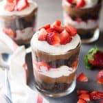 A chocolate brownie trifle in a glass layered with brownies, chocolate pastry cream and whipped cream, and fresh strawberry.