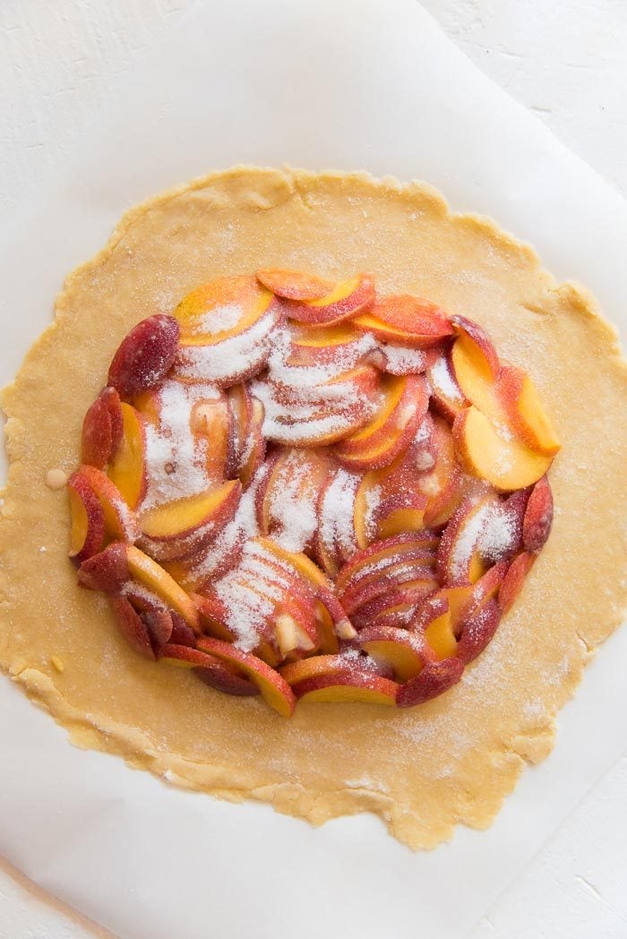 Sprinkle the sugar all over the fresh peaches. This will create the glaze in the peach galette. Make sure there is a border in the pie crust.