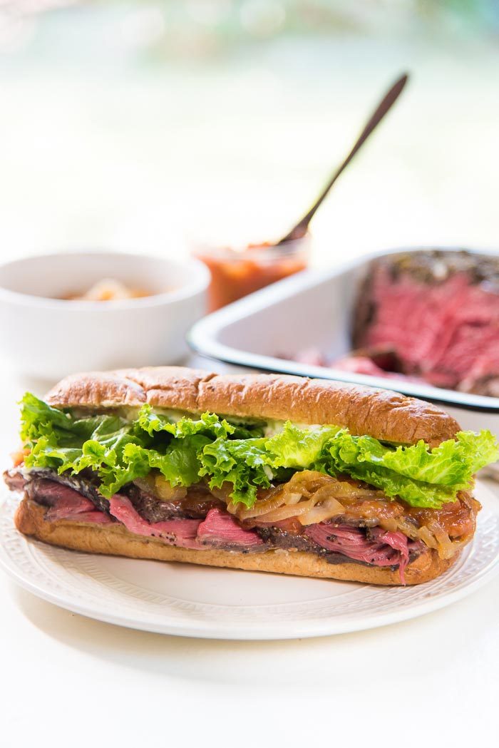 A steak sandwich on a white plate. Whole wheat bread buns, filled with thinly sliced beef, caramelized onion, peach relish, salad leaves and mayonnaise. You can substitute the fillings with any fillings your prefer. 