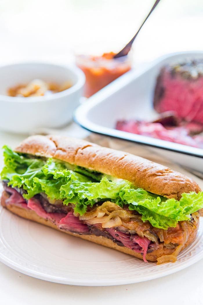 A close up of the Steak sandwich with rare cooked, slow roasted spiced beef, with the slow roast beef, caramelized onion and peach relish in the background. Substitute with roasted peppers, red onions, arugula leaves, fruit chutney or any filling that you like. 