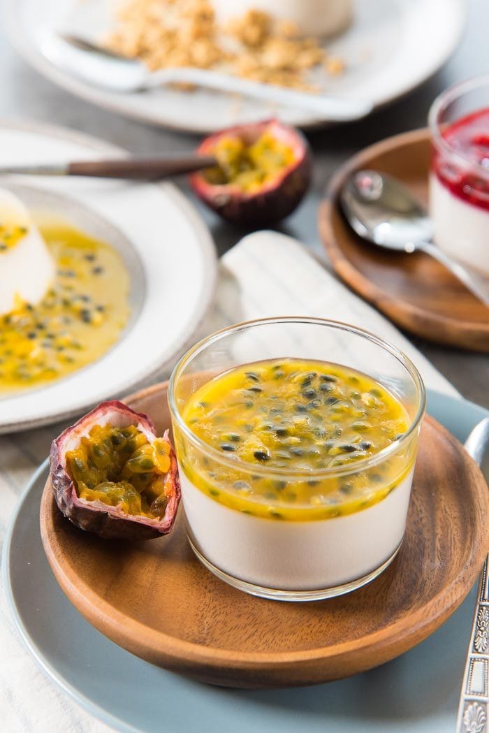 A Passion fruit topped Coconut panna cotta served in a glass, with half a fresh passion fruit next to it. 