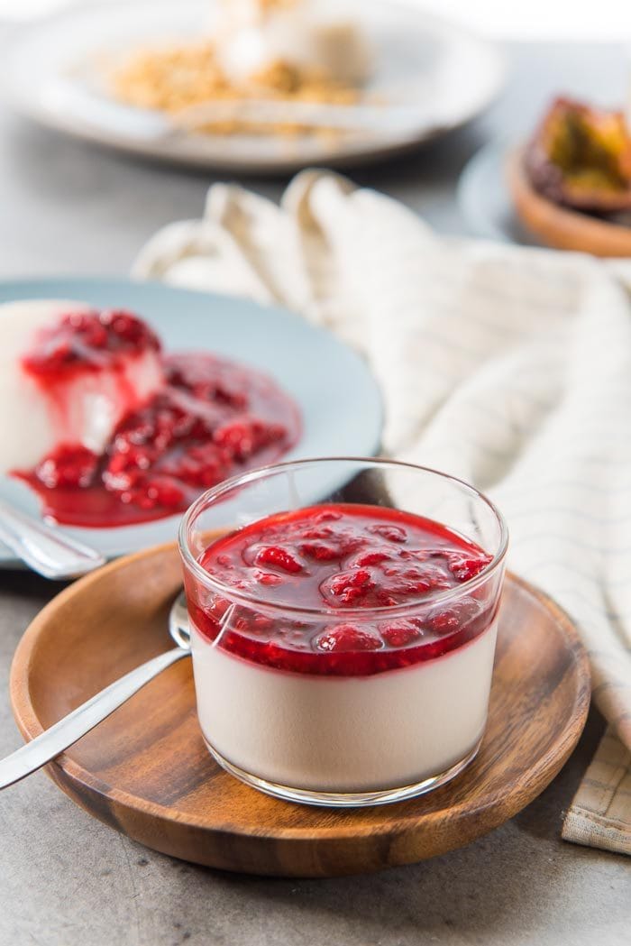Raspberry topped coconut panna cotta served in a glass kept on a small wooden plate.