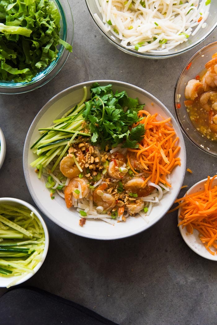 Assembling Garlic Lime Shrimp Rice noodle salad. Top it all with spring onions, roasted peanuts and cilantro and extra dressing.