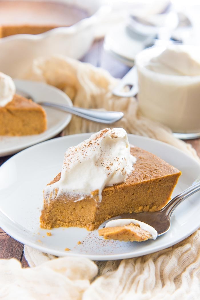 A slice of crustless pumpkin pie slice with a bite take out, served on a white plate with a spoon next to it. 