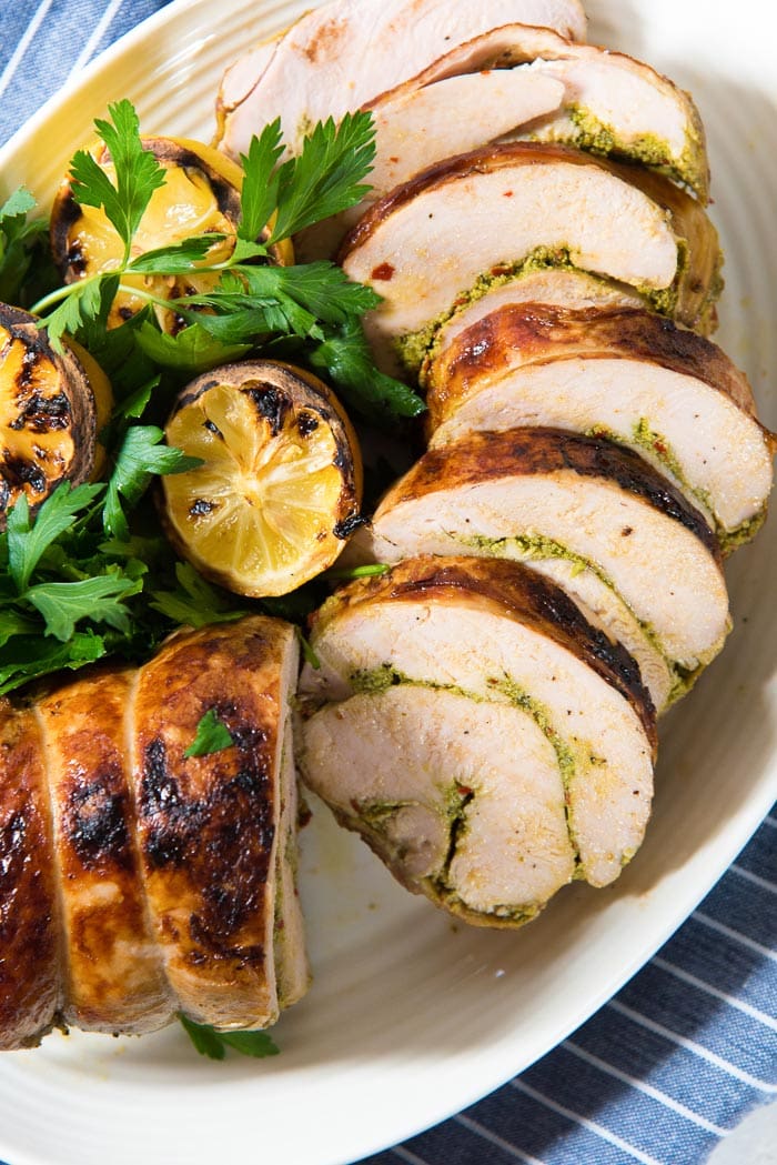An overhead view of the sliced sous vide thanksgiving turkey roulade on a serving platter with grilled lemons and herb garnishes.