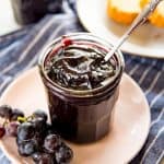 Homemade concord grape jam in a glass jar with a bunch of grapes on the side.