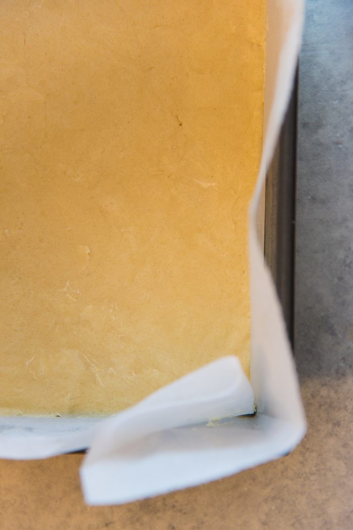Shortbread crust pressed into a parchment lined pan, before being baked. 