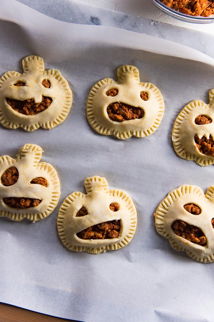 Unbaked pumpkin shaped hand pies on a baking tray before being baked.