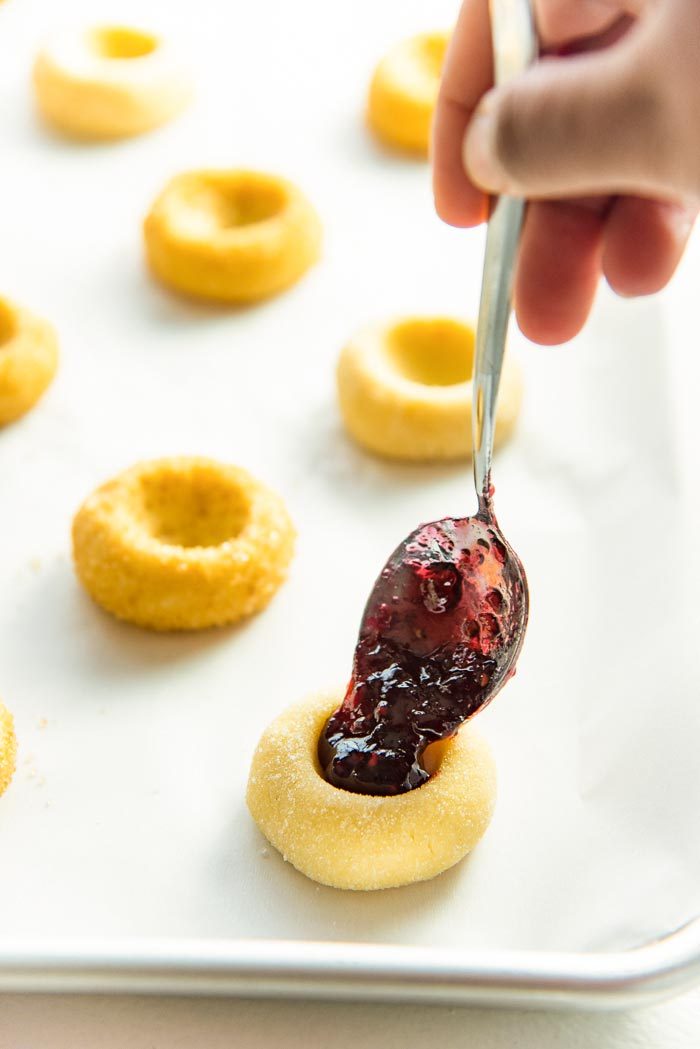 The thumbprint cookies shaped and placed on a baking tray with the centers being filled with raspberry jam. 