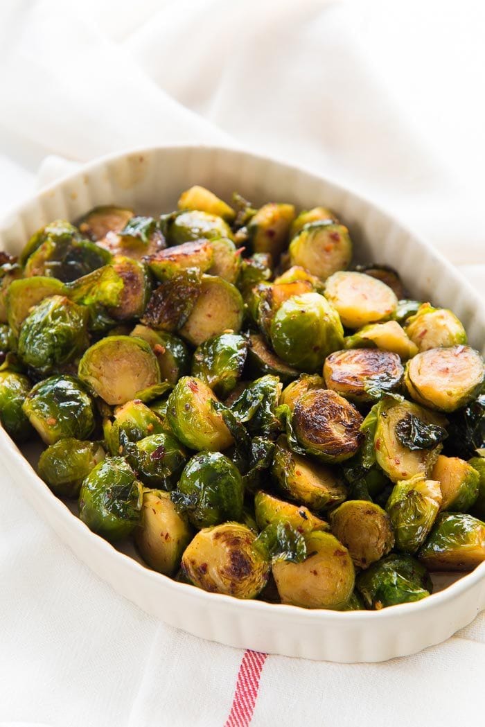 Maple roasted Brussels sprouts in a white oval dish, on a white table top. 