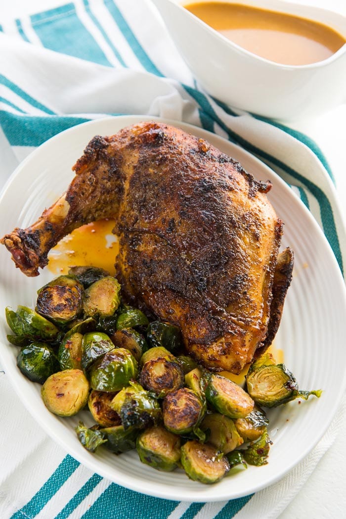 Cajun Roasted Turkey Breast on a white platter with roasted brussels sprouts on the side, and gravy in a gravy boat in the background.