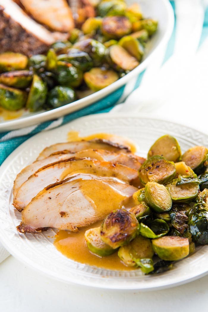 A close up of the Thanksgiving plate with gravy poured oven roasted turkey breast slices and roasted brussels sprouts on the side. 