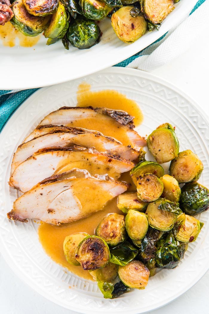 An overhead view of a Thanksgiving plate with juicy slices of turkey breast roast and roasted brussels sprouts