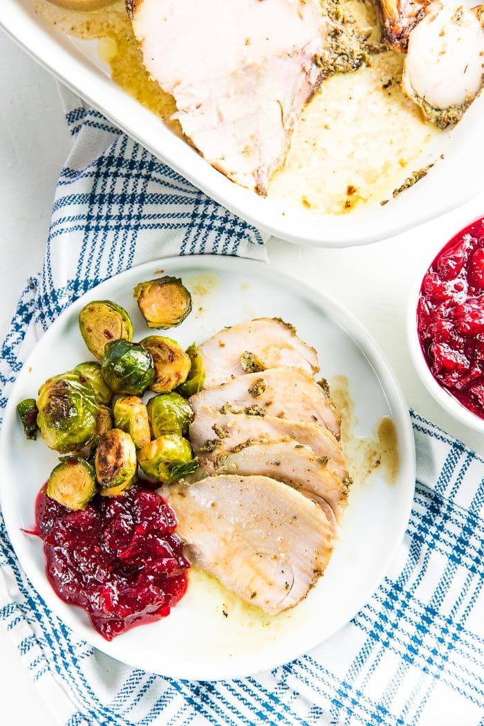 An overhead view of slices of juicy turkey breast served on a white plate with cranberry sauce and brussels sprouts.
